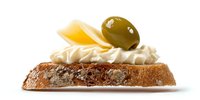 Gourmet appetizer with cream cheese, olive, and cheese slice on rustic bread slice, perfect for catering and restaurant menus.