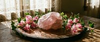 Rose quartz crystal surrounded by pink roses on vintage tray creates serene spa atmosphere for meditation and healing practices.