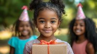 Young African American girl with curly hair smiling while holding wrapped present at outdoor birthday party celebration, wearing festive party hat with friends in background.