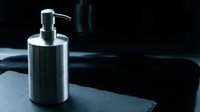 Stainless steel soap dispenser on dark granite countertop in modern bathroom interior with dramatic lighting and shadows creating luxury spa atmosphere.