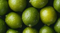 Fresh green limes with water drops on dark background, macro shot of citrus fruits showing textured peel and natural moisture for food and beverage designs.