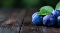 Fresh ripe plums with water drops and green leaves on rustic wooden background, selective focus with natural lighting and copy space for text.