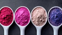 Vibrant cosmetic pigment powders in measuring spoons showing gradient from deep red to purple, natural mineral makeup ingredients on dark background.
