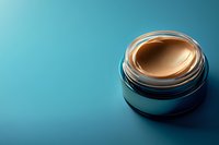 Luxurious cream foundation in opened silver jar against turquoise background with dramatic lighting and copy space for beauty and cosmetic marketing.