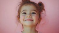 Adorable young Asian girl with pigtails smiling joyfully against soft pink background. Happy child portrait expressing pure joy and innocence for family content.