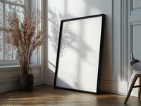 Black frame mockup leaning against white wall with natural sunlight casting tree shadows, dried pampas grass in vase on herringbone wooden floor. Interior design display.