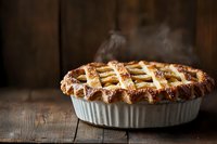 Freshly baked apple pie with golden lattice crust steaming on rustic wooden table, homemade pastry in white ceramic dish with flaky, crispy edges.