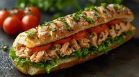 Fresh tuna salad submarine sandwich with lettuce, tomatoes and herbs on crusty baguette, close up view on dark background with ingredients.