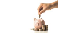 Hand dropping coin into pink piggy bank with stacked coins on white background for savings and financial planning concepts.