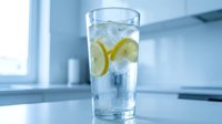 Refreshing glass of cold water with lemon slices and ice cubes on a white kitchen counter, blue tones, healthy hydration concept.