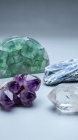 Collection of healing crystals and gemstones including green fluorite, purple amethyst, blue kyanite and clear quartz on neutral background for wellness.