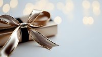 Elegant champagne-colored satin bow with glitter trim on gift box against soft bokeh background, creating luxurious festive mood for special occasions and celebrations.