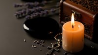 Mystical altar setup with burning candle, obsidian scrying mirror, ankh symbol and wooden box for spiritual practices and divination rituals.