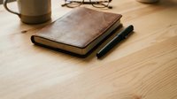 Brown leather notebook with pen on wooden desk workspace with coffee cup and glasses for business planning and writing.