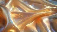 Luxurious golden silk fabric with soft folds and shimmering light effects creates elegant waves and curves, highlighting rich texture and luminous surface.