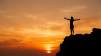 Silhouette of person with raised arms celebrating success on mountain peak during golden sunset sky for motivation and achievement concepts.