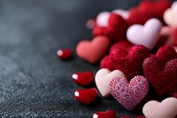 Red and pink glittery hearts scattered on dark textured surface for Valentine's Day romantic celebration and love themed designs.