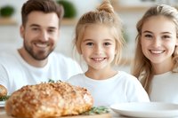 Happy Caucasian family with young daughter smiling at dining table with fresh baked bread, expressing joy and togetherness during mealtime at home.