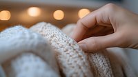 Gentle fingers touching soft knitted fabric texture with warm bokeh lights in background, creating cozy winter atmosphere and highlighting delicate wool pattern.