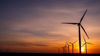 Wind turbines silhouetted against dramatic sunset sky with orange and purple clouds, renewable energy farm generating clean electricity at dusk.