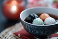Colorful traditional Asian dumplings in black ceramic bowl with textured pattern, served on red napkin. Soft candlelight creates cozy dining atmosphere.