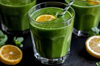 Fresh green smoothie with spinach, citrus and herbs in glass. Healthy detox drink garnished with orange slice and metal straw on dark background.