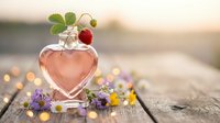 Heart-shaped glass bottle with pink liquid and strawberry on rustic wooden surface surrounded by wildflowers at golden hour sunset.