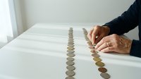 Senior adult hands arranging coins in organized rows on white surface, financial planning and savings concept for banking, investment, wealth management and retirement planning.