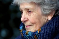 Senior Caucasian woman with silver hair wearing blue knitted scarf looking away pensively, side profile portrait showing natural aging and wisdom.