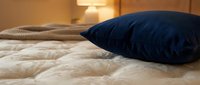 Cozy bedroom scene with navy blue pillow on quilted beige bedding, warm ambient lighting, and knit throw blanket for home decor and interior design use.