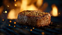 Juicy grilled beef steak with seasoning and spices on dark background with fire flames and bokeh lights. Close up view of medium rare meat cooking.