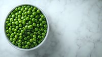 Fresh green peas in white ceramic bowl on marble background with copy space. Top view of organic vegetables for healthy eating and cooking.