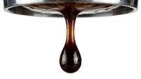 Thick liquid dripping from metal spoon, rich brown syrup or honey drop forming on white background, cooking and food preparation ingredient.