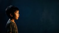 Young Asian boy in profile against dark blue background, wearing casual clothing, suitable for educational materials, child development concepts, and diversity representation.