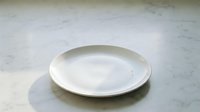 Empty white ceramic plate on marble surface, suitable for food styling, restaurant menus, culinary blogs, and tableware design projects.
