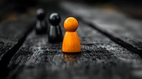 Orange wooden figure standing out among black figures on dark wooden surface, selective color highlighting uniqueness and leadership concept.