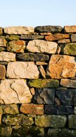 Ancient dry stone wall with weathered limestone blocks and moss patches creating rustic texture against clear sky for construction and heritage projects.
