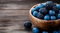 Fresh ripe blackberries and blueberries in wooden bowl on rustic dark table, selective focus with copy space for healthy eating concept.