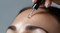 Young Asian woman receiving facial serum treatment with dropper applicator, close-up view showing skincare routine and cosmetic application on forehead.