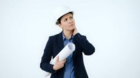 Young male architect or engineer of mixed ethnicity wearing white hard hat and dark blazer, holding rolled blueprints, looking upward thoughtfully against white background for construction and professional design projects.