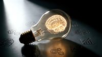 Glowing light bulb with brain filament on business documents with charts and graphs representing innovation, creativity and intelligent solutions for corporate strategy.