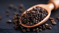 Fresh dark cacao nibs in wooden spoon on black background, raw chocolate pieces scattered around, macro food photography for culinary and healthy eating.