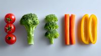 Fresh colorful vegetables arranged in neat rows on white background - cherry tomatoes, broccoli florets, carrot sticks and yellow bell pepper slices for healthy eating concept.