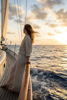 Young woman with flowing hair enjoying sunset sailing adventure on luxury yacht deck with golden sky and ocean waves for travel lifestyle content.