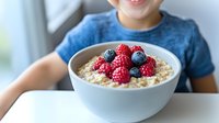 Healthy breakfast bowl with oatmeal porridge topped with fresh raspberries and blueberries. White ceramic bowl on table shows nutritious morning meal.