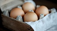 Fresh brown chicken eggs in rustic cardboard carton with soft natural lighting, shallow depth of field creates artisanal food photography mood.