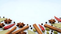 Aromatic spices scattered on white background with cinnamon sticks, star anise, cardamom pods and chili peppers for culinary and cooking projects.