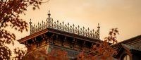 Ornate Victorian rooftop with decorative iron cresting and finials against warm sunset sky. Historic architectural detail showcasing craftsmanship and period design elements.