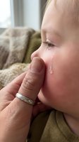 Caring parent gently wipes a tear from a crying toddler's cheek, capturing a tender moment of comfort and parental love at home.