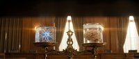 Elegant brass candelabra with ornate glass holders displaying decorative patterns in warm candlelight against luxurious curtained interior background.